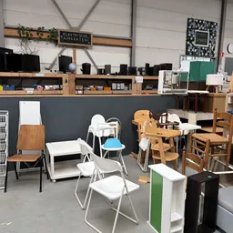Winkelvloer met diverse meubels: houten stoelen, witte kunststofstoelen, een kinderbed, houten kasten en andere tweedehands a