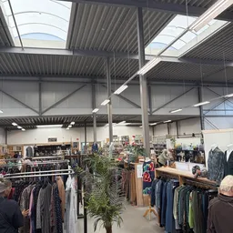 Ruim magazijn met kledingrekken, stellingen en artikelen verdeeld over verschillende afdeling