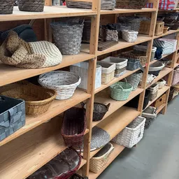 Houten stellingen vol met verschillende soorten manden, tassen en opbergdozen in diverse kleuren en materialen