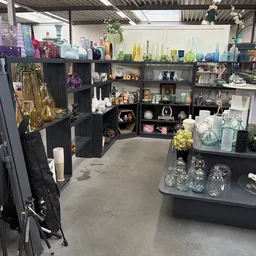 Zwarte stellingen met diverse huishoudelijke spullen, glaswerk, vazen en decoratieartikelen in een kringloopwinkel