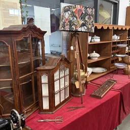 Antieke meubels en huishoudelijke items uitgestald in een kringloopwinkel, waaronder houten kasten met glasdeuren, servies en