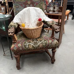 Houten stoel met groene tapijtstof bekleding en rieten mand met witte doek en rode bal erop