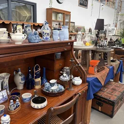 Verzameling vintage en antieke servies, vazen en decoratieve items op houten kasten en tafels