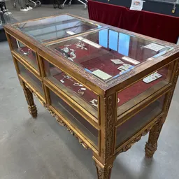 Antieke vitrinekast met gouden houten frame en glazen deuren, gevuld met decoratieve voorwerpen op rode achtergrond