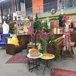 Ingericht interieur met vintage meubels, bloemen in vaas, gele tafel en bruine fauteuils in kringloopwinkel