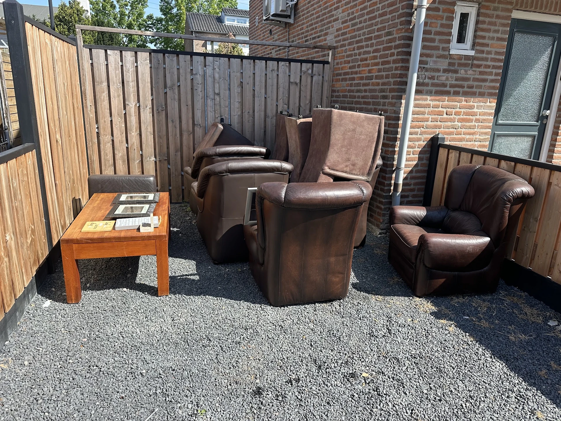 Bruinleren fauteuils en stoelen uitgestald op een grindterras naast een houten tafel