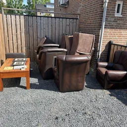 Bruinleren fauteuils en stoelen uitgestald op een grindterras naast een houten tafel