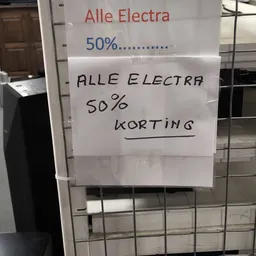 Handgeschreven tekst op papier geplakt op een raam: '50%.......... ALLE ELECTRA 50% KORTING'