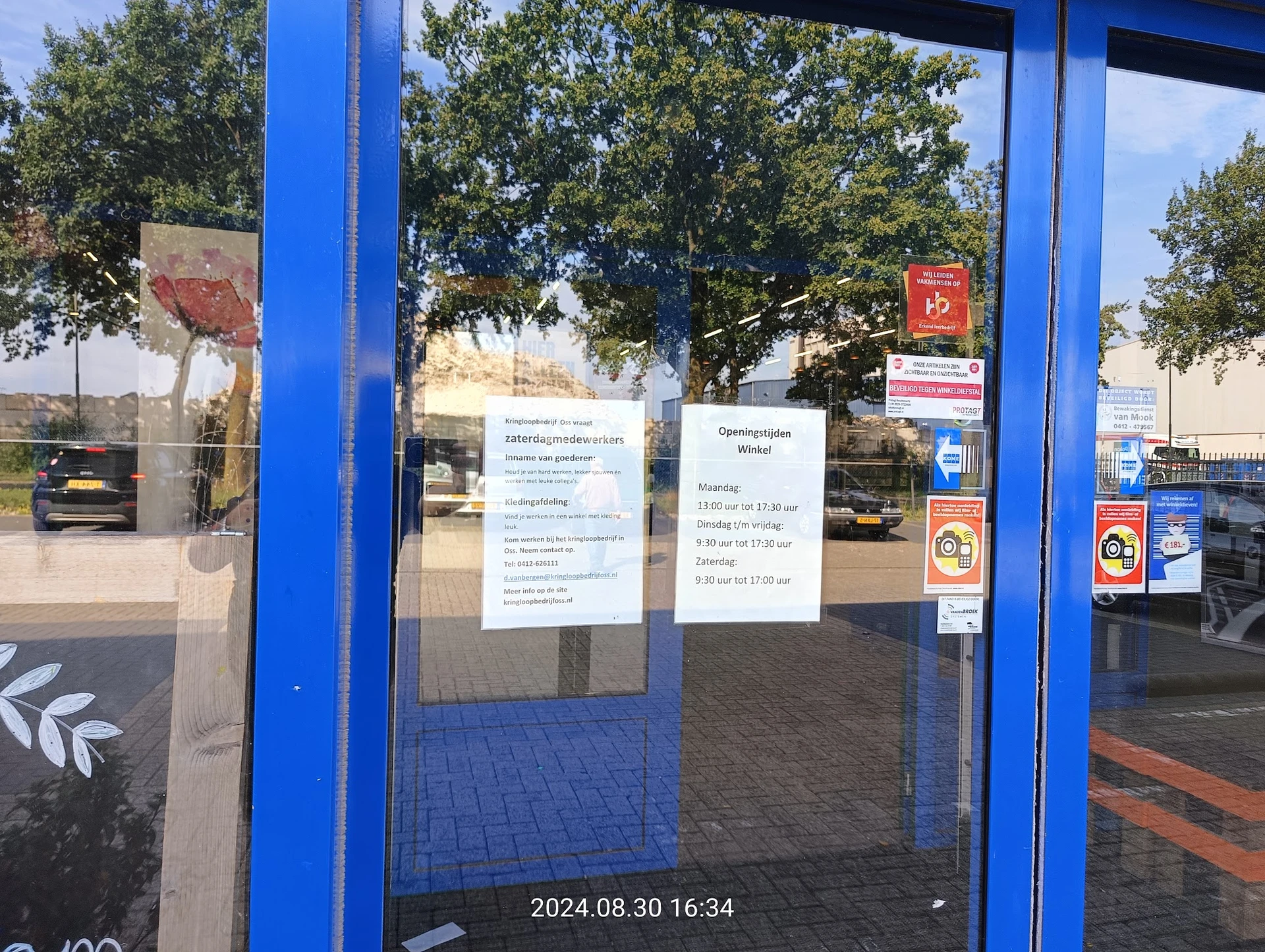Blauwe deur met glazen pui en informatiekaarten eraan geplakt, parkeerplaats op achtergrond