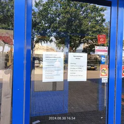 Blauwe deur met glazen pui en informatiekaarten eraan geplakt, parkeerplaats op achtergrond