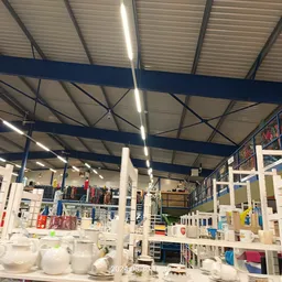 Ruim winkelinterieur met stellingen, witte serviesgoed in voorgrond, blauwe balken aan plafond, gekleurde bakken en spullen o