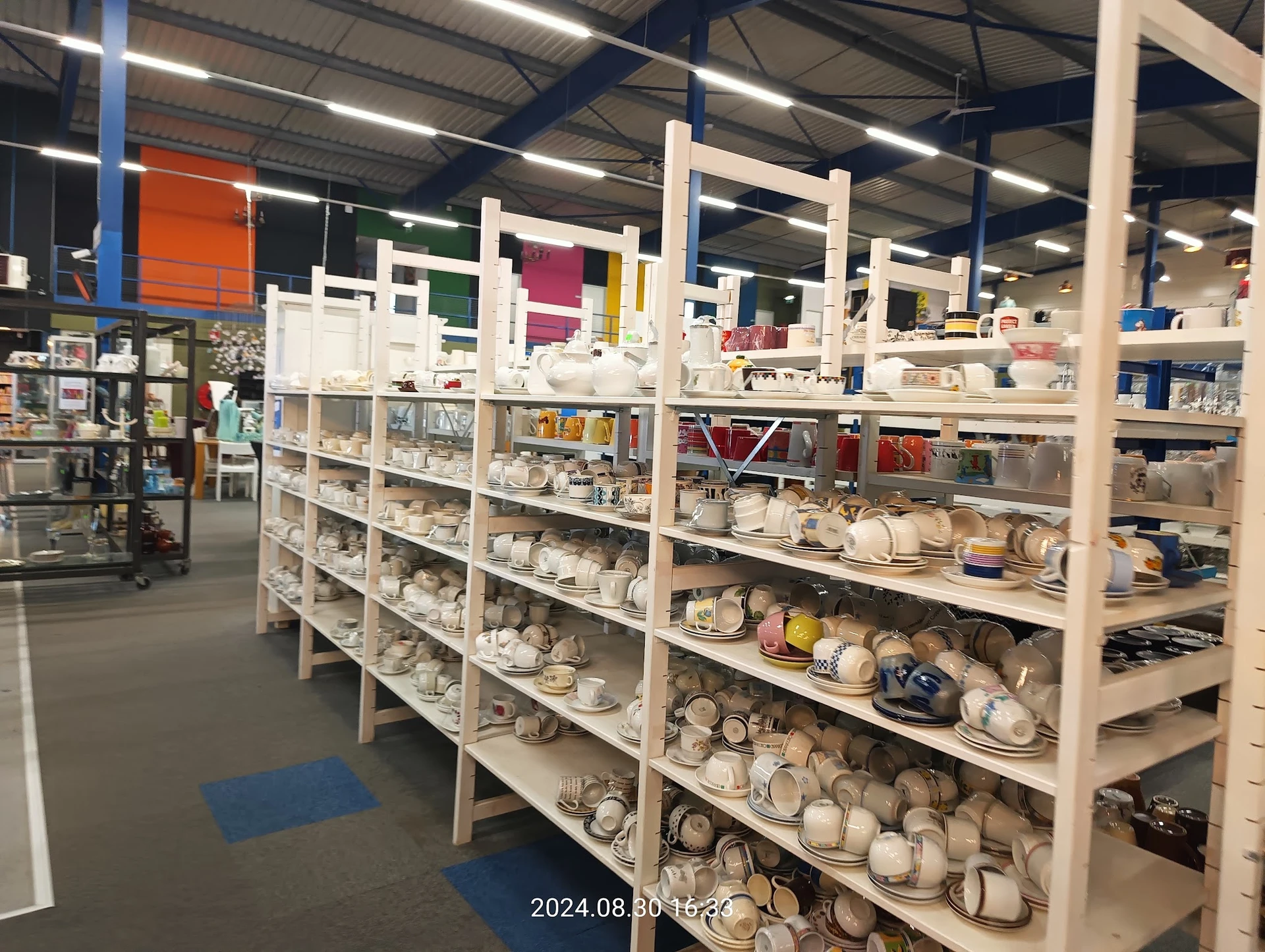 Uitgebreide stellingen met serviesgoed, kopjes, borden en ander huishoudelijke artikelen in een kringloopwinkel