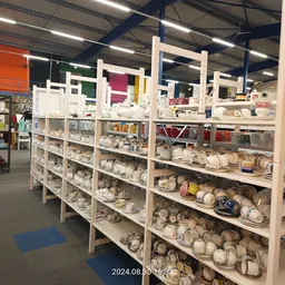 Uitgebreide stellingen met serviesgoed, kopjes, borden en ander huishoudelijke artikelen in een kringloopwinkel