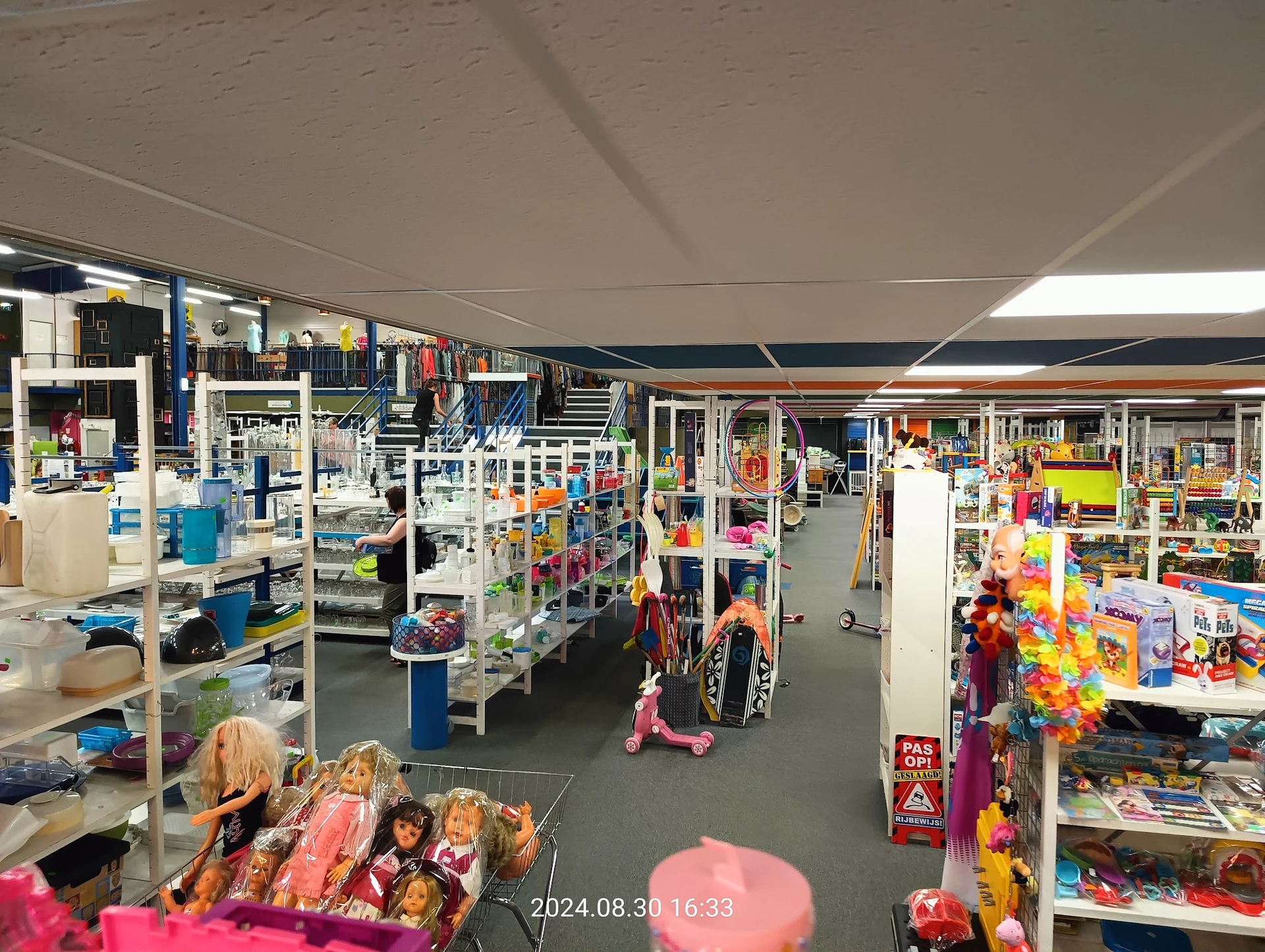 Overzicht van de winkelhal met diverse stellingen vol speelgoed, poppen en kinderspullen langs de zijkanten