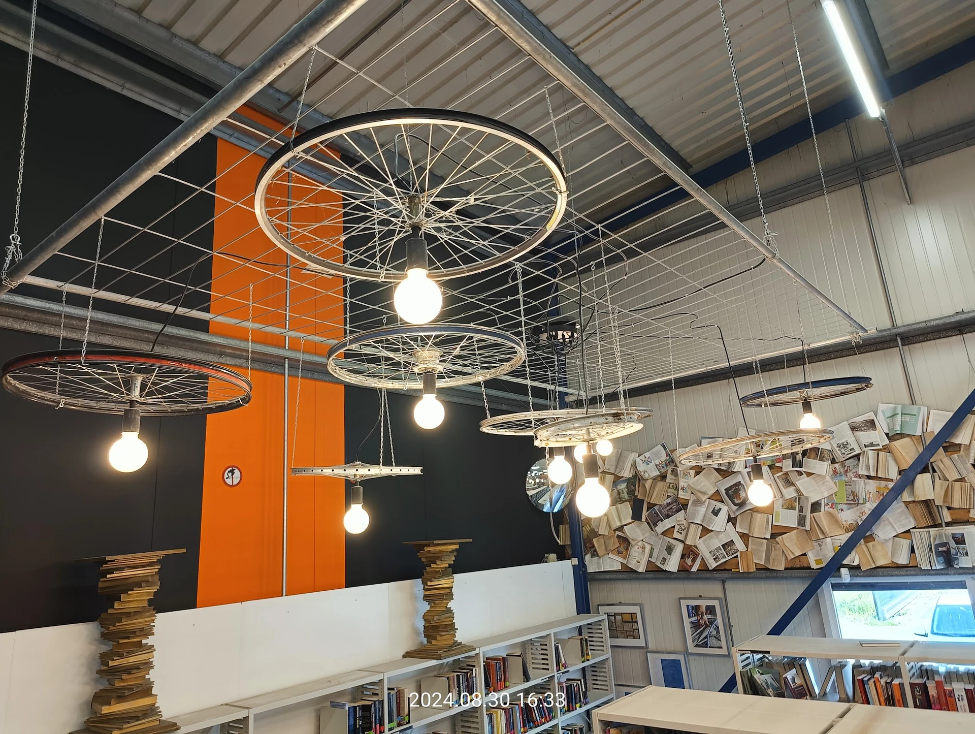Plafond van kringloopwinkel met decoratieve fietswiellampen en oranje muur met boekenkasten