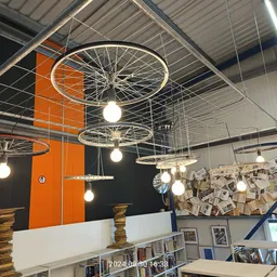 Plafond van kringloopwinkel met decoratieve fietswiellampen en oranje muur met boekenkasten