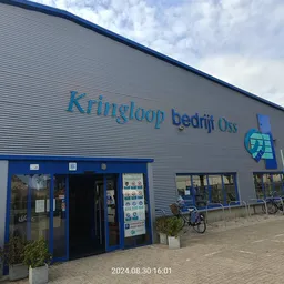 Gevel van kringloopwinkel met blauwe deuren en ramen, fietsen geparkeerd ervoor
