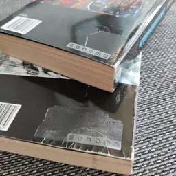 Gestapelde boeken en items op een donkere tafel, deels in plastic verpakt