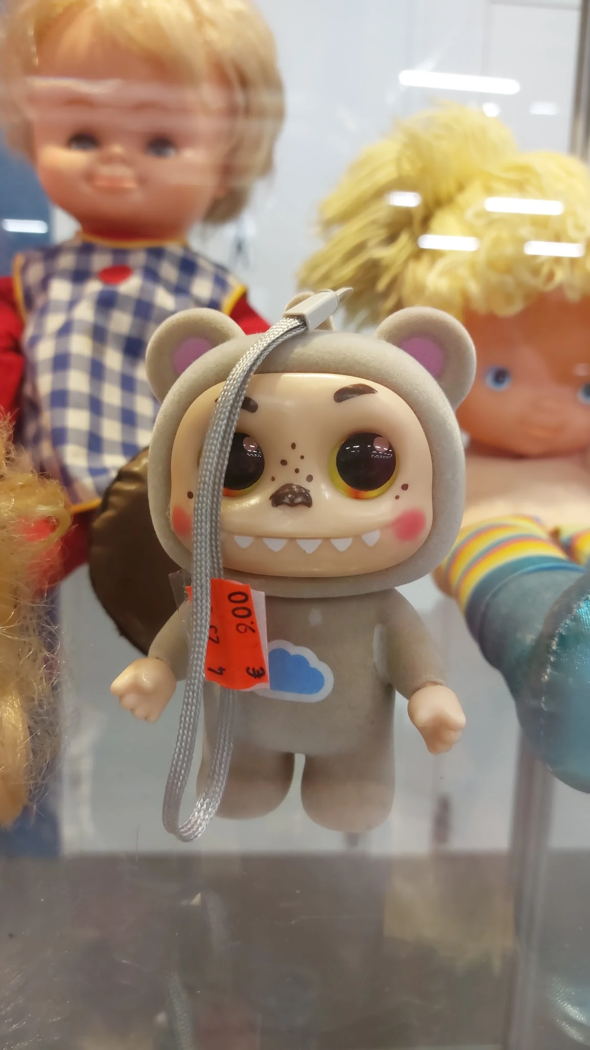 Close-up van een speelgoedbeertje met grote ogen en getande mond, met een grijs oorbandje