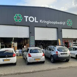 Grijze gevel van kringloopbedrijf TOL met groene recycle-logo's en drie open roldeurendeuren, parkeerplaats met auto's ervoor