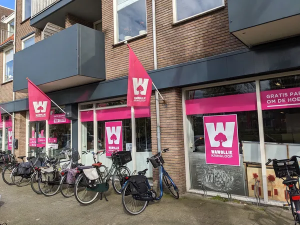 Gevel van kringloopwinkel met roze logo's en uithangborden, fietsen geparkeerd voor de ingang