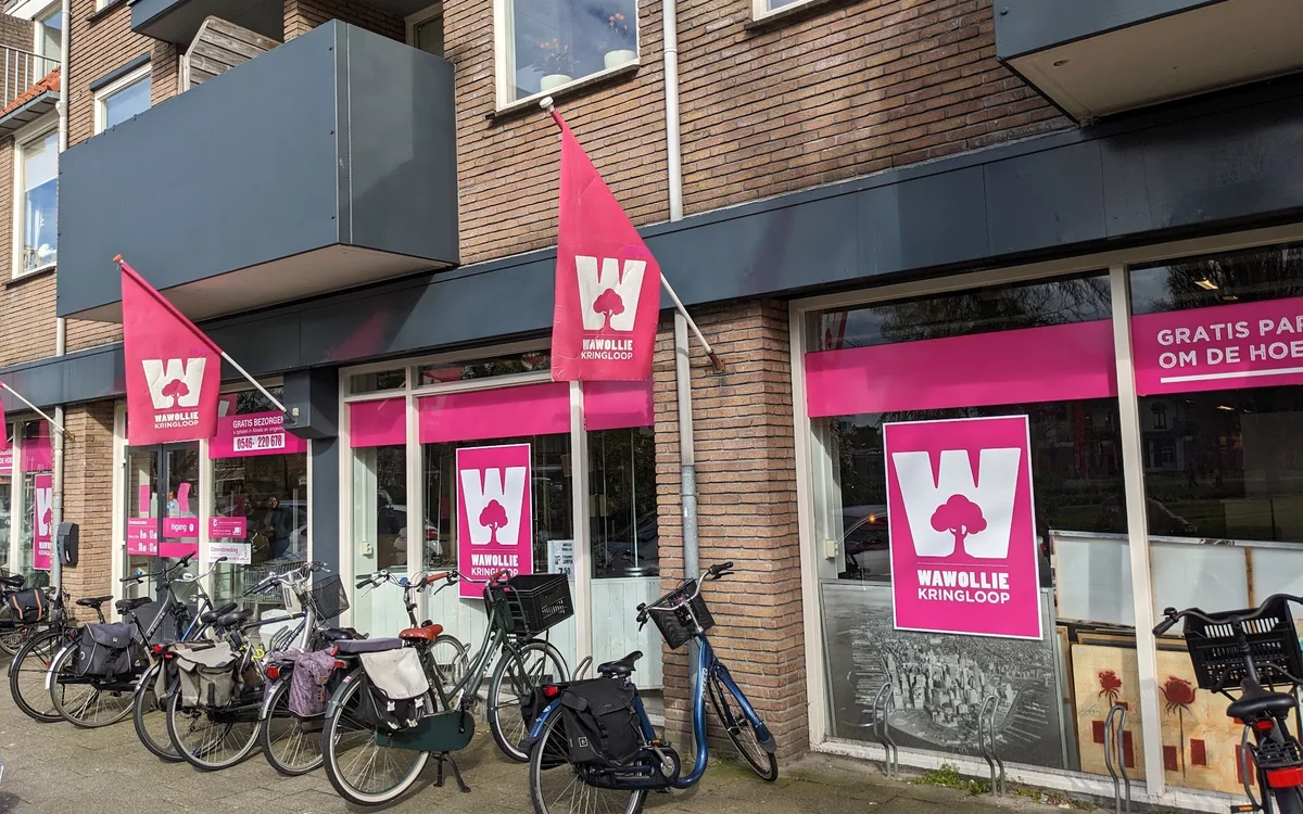 Gevel van kringloopwinkel met roze logo's en uithangborden, fietsen geparkeerd voor de ingang
