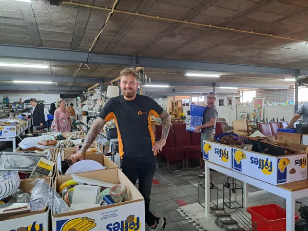 Mannelijke medewerker in kringloopwinkel tussen dozen en uitgestalde spullen op tafels