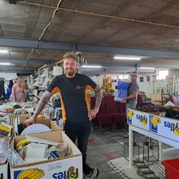 Mannelijke medewerker in kringloopwinkel tussen dozen en uitgestalde spullen op tafels