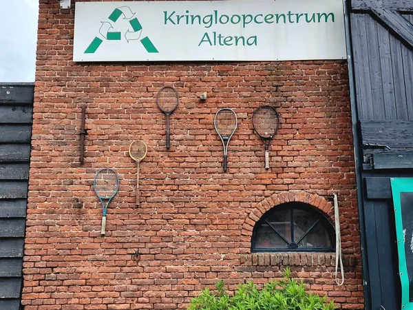 Bakstenen gevel met Kringloopcentrum Altena-logo en decoratieve tennisrackets aan de muur