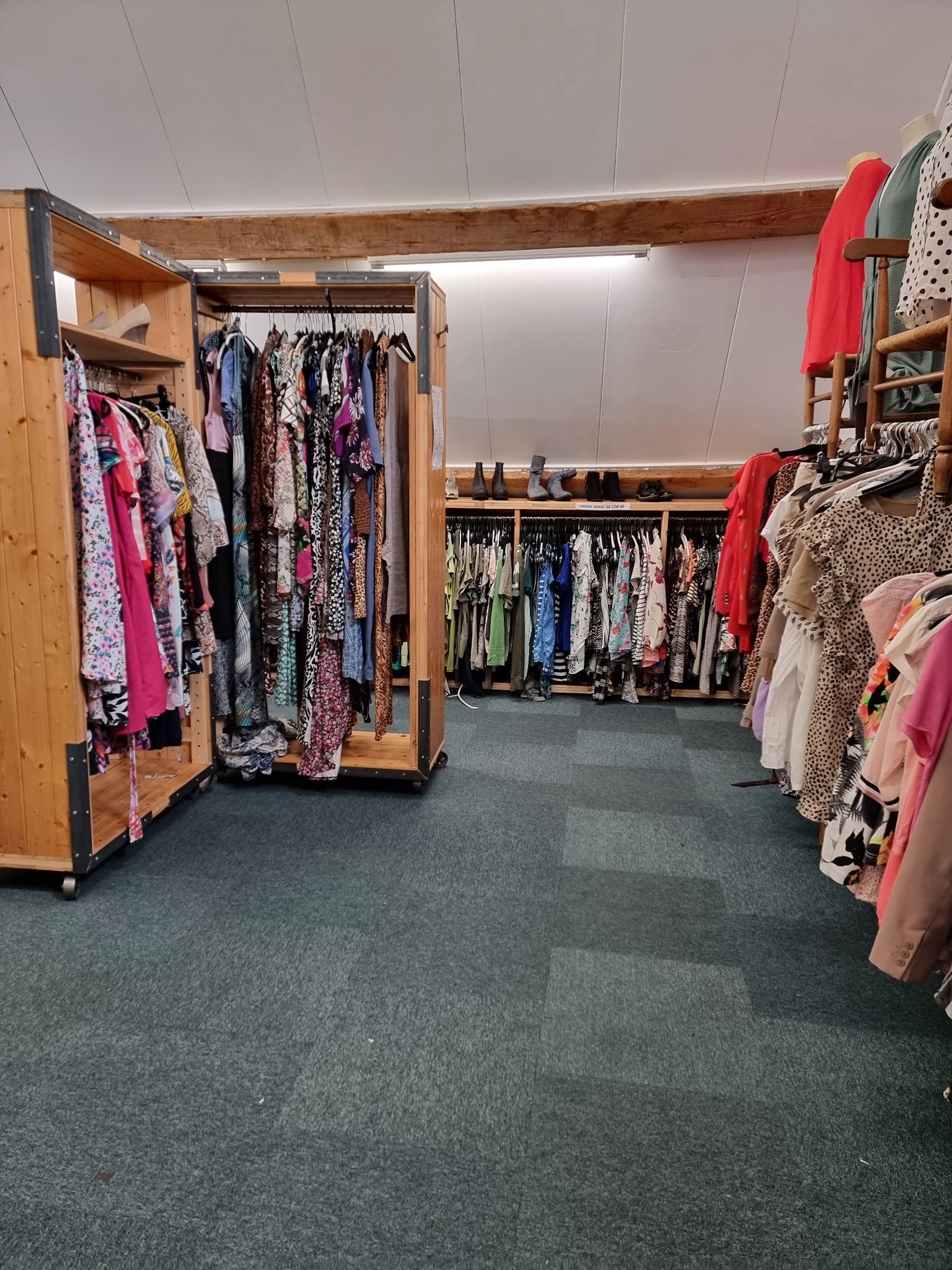 Rekken met tweedehands dameskleding, waaronder jurken, blouses en andere kledingstukken in verschillende kleuren