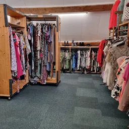 Rekken met tweedehands dameskleding, waaronder jurken, blouses en andere kledingstukken in verschillende kleuren