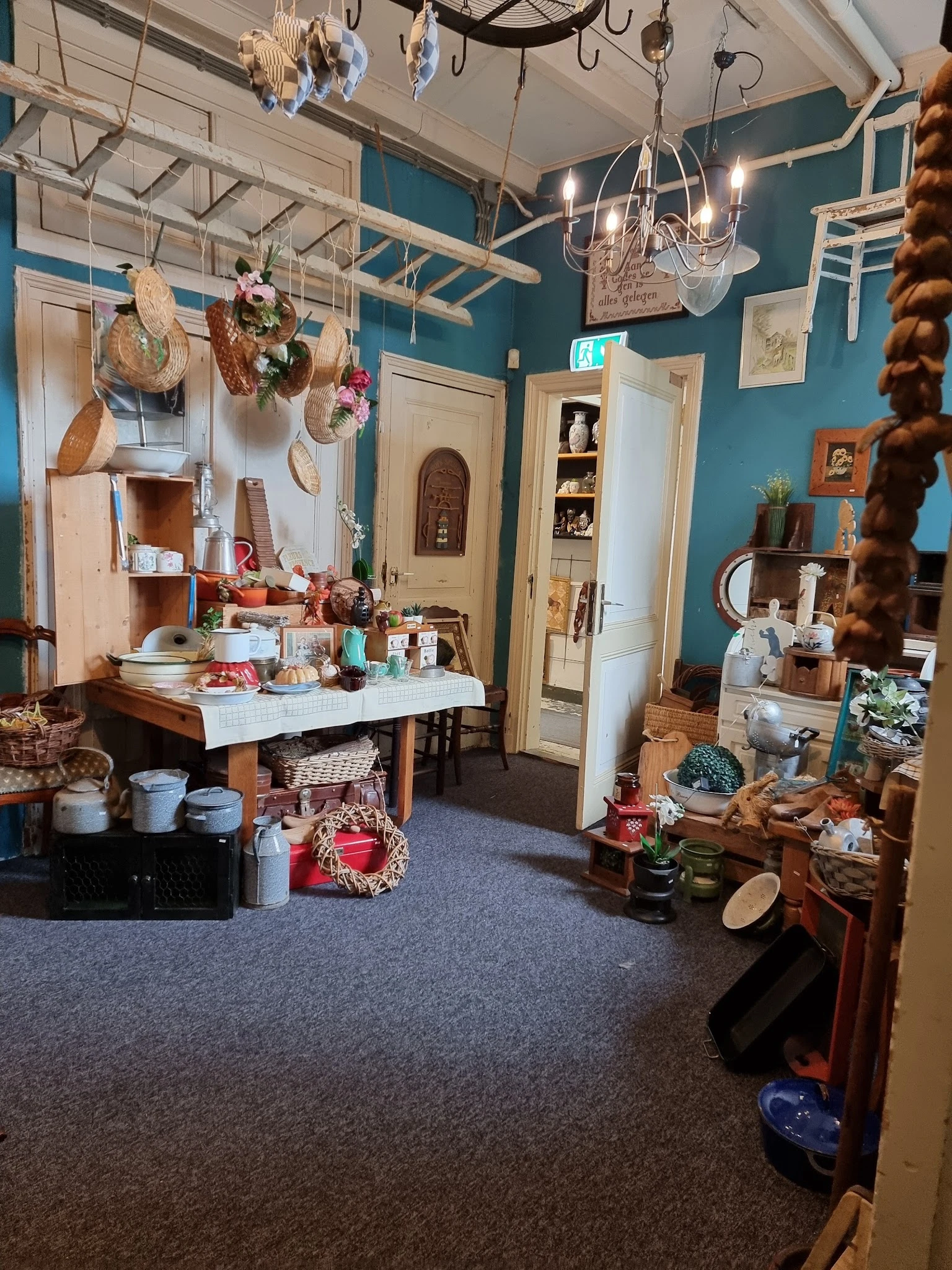 Winkelbinnenruimte met turquoise wanden, houten deuren, stellingen met huishoudelijke artikelen, decoratiestukken en diversen