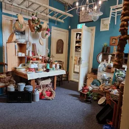 Winkelbinnenruimte met turquoise wanden, houten deuren, stellingen met huishoudelijke artikelen, decoratiestukken en diversen