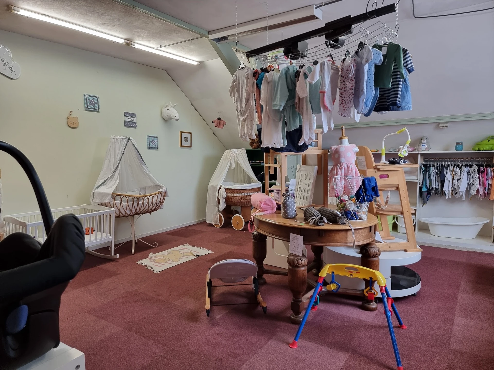 Babyafdeling met wiegjes, kinderkledingrek, speelgoed en drogende babykleding onder lampje