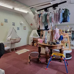 Babyafdeling met wiegjes, kinderkledingrek, speelgoed en drogende babykleding onder lampje