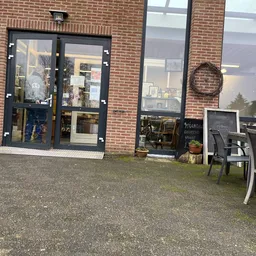 Bakstenen gevel van kringloopwinkel met zwarte deur, ramen en terras met stoelen