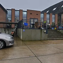 Voorkant kringloopwinkel met parkeerplaats, trap en ingang zichtbaar