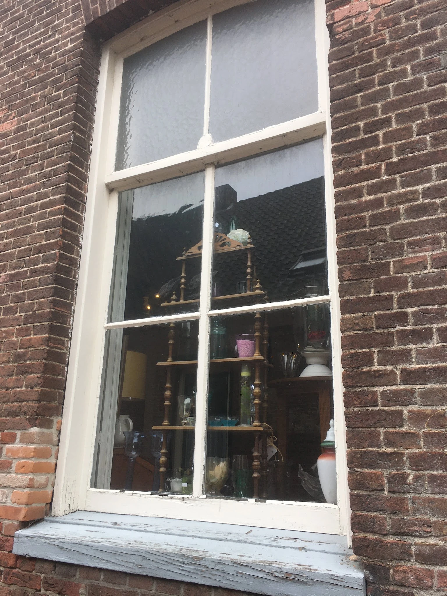 Binnenkant van een raam met daarachter houten stellingen met diverse artikelen en decoratieve spullen.