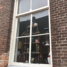 Binnenkant van een raam met daarachter houten stellingen met diverse artikelen en decoratieve spullen.