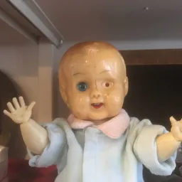 Vintage poppenhoofd met blond haar en blauwe ogen, gekleed in lichtblauw en roze kledingje