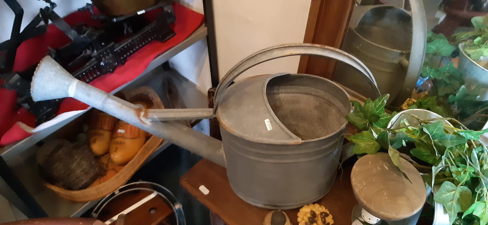 Grijze metalen gieter met deksel en handvat op een houten tafel