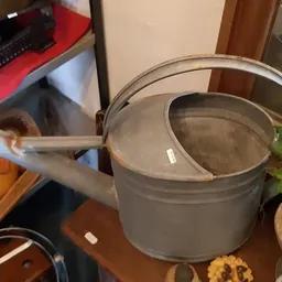 Grijze metalen gieter met deksel en handvat op een houten tafel