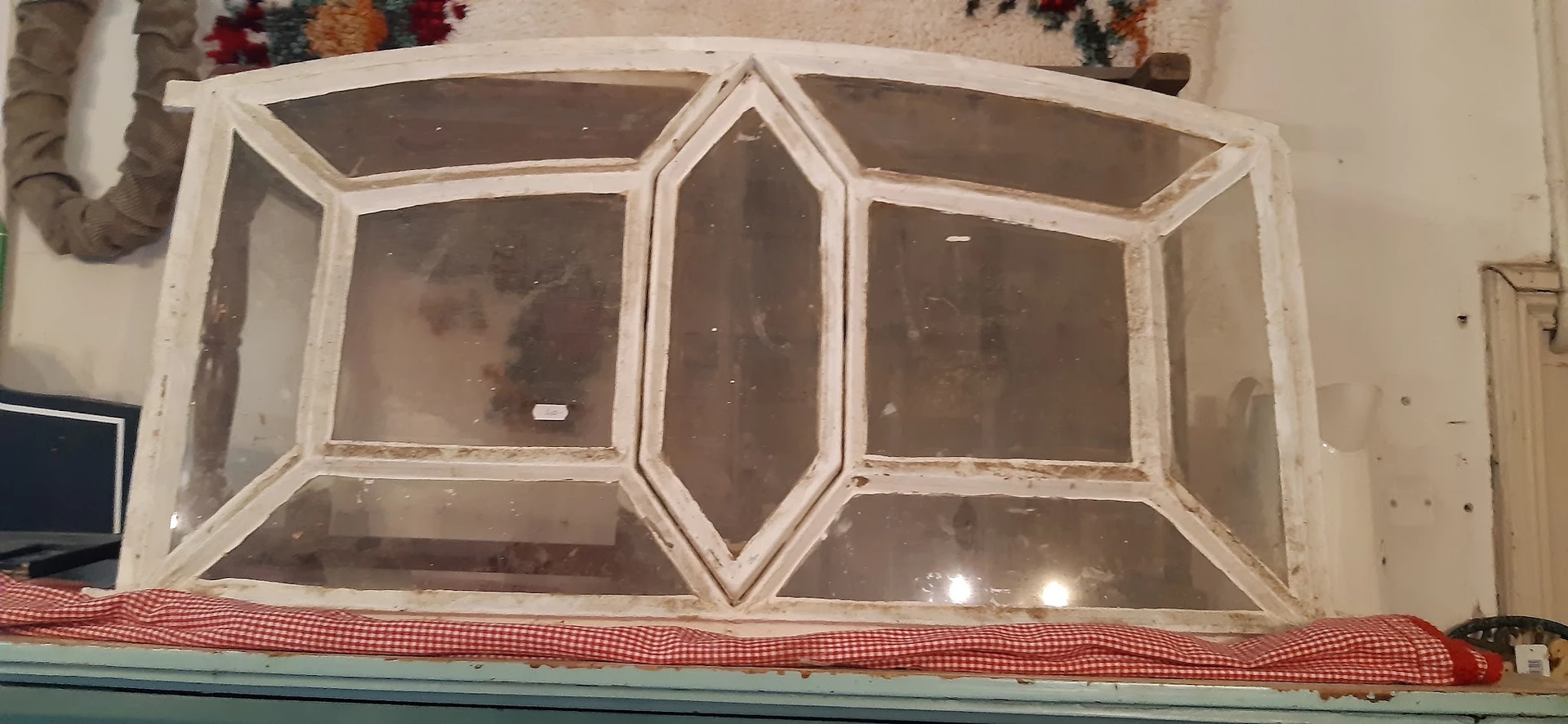 Wit houten raamkozijn met zes panelen en centrale decoratieve vorm, tegen een muur