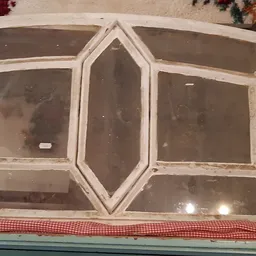 Wit houten raamkozijn met zes panelen en centrale decoratieve vorm, tegen een muur