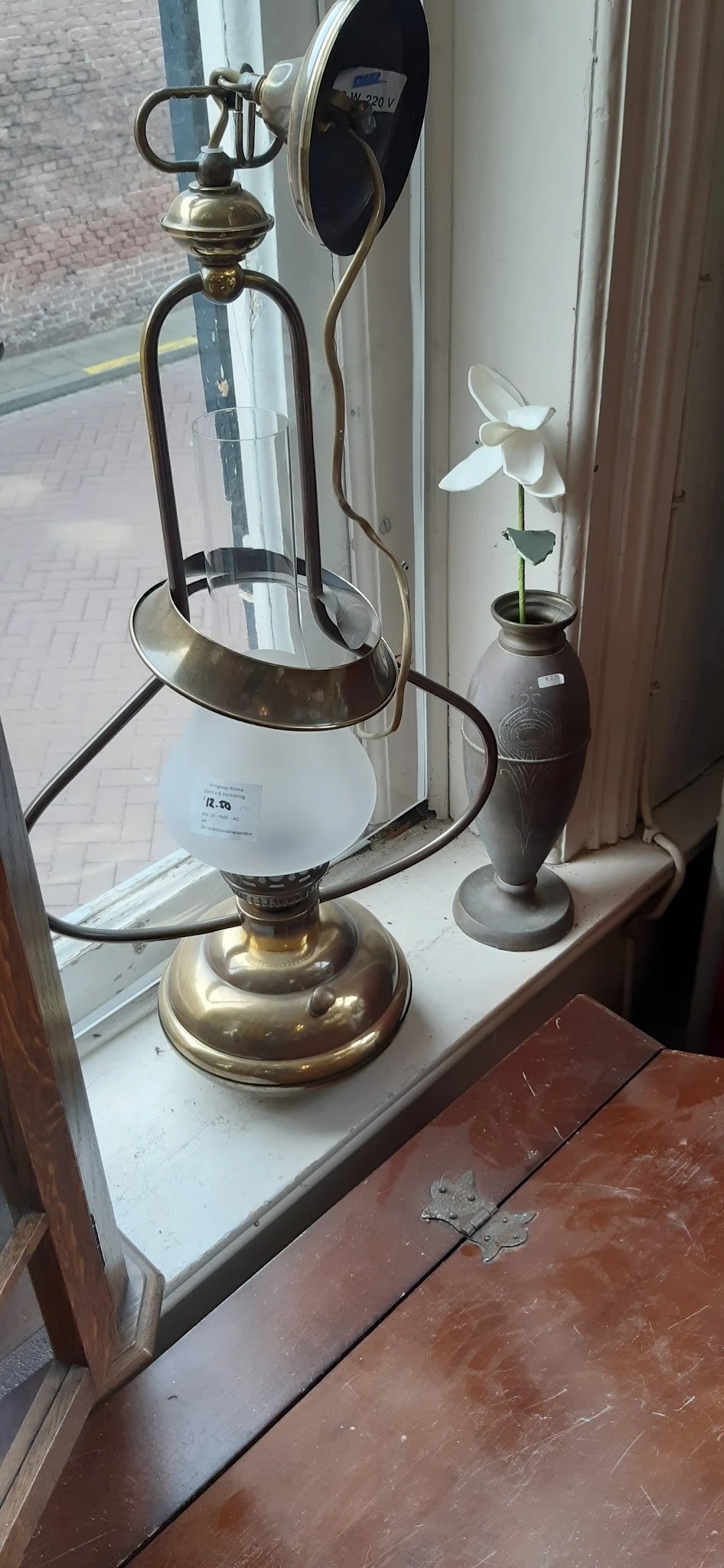 Twee vintage lampen op een vensterbank: een messing tafellamp met wit glazen kap en een donkere vaasachtige lamp met plantje