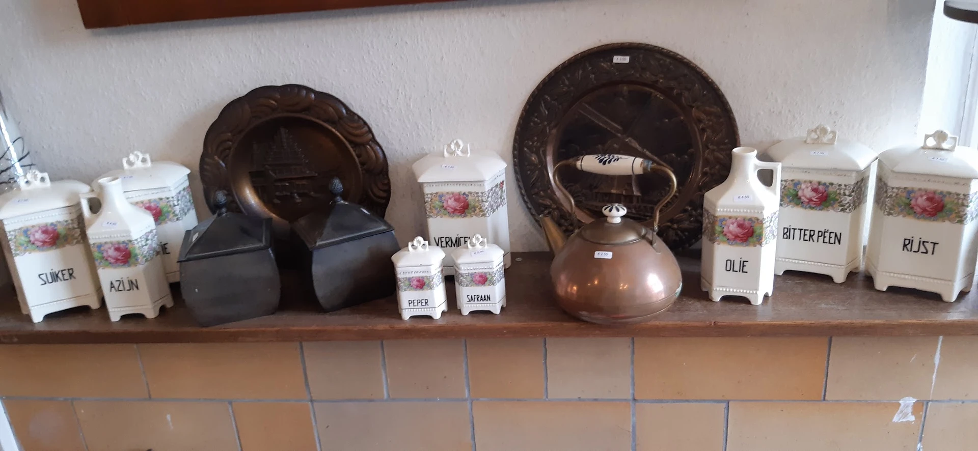 Stellingkast met bruine decoratieve borden, koperen theepot, potjes met kruiden en witte porseleinen items