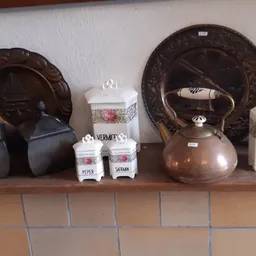 Stellingkast met bruine decoratieve borden, koperen theepot, potjes met kruiden en witte porseleinen items