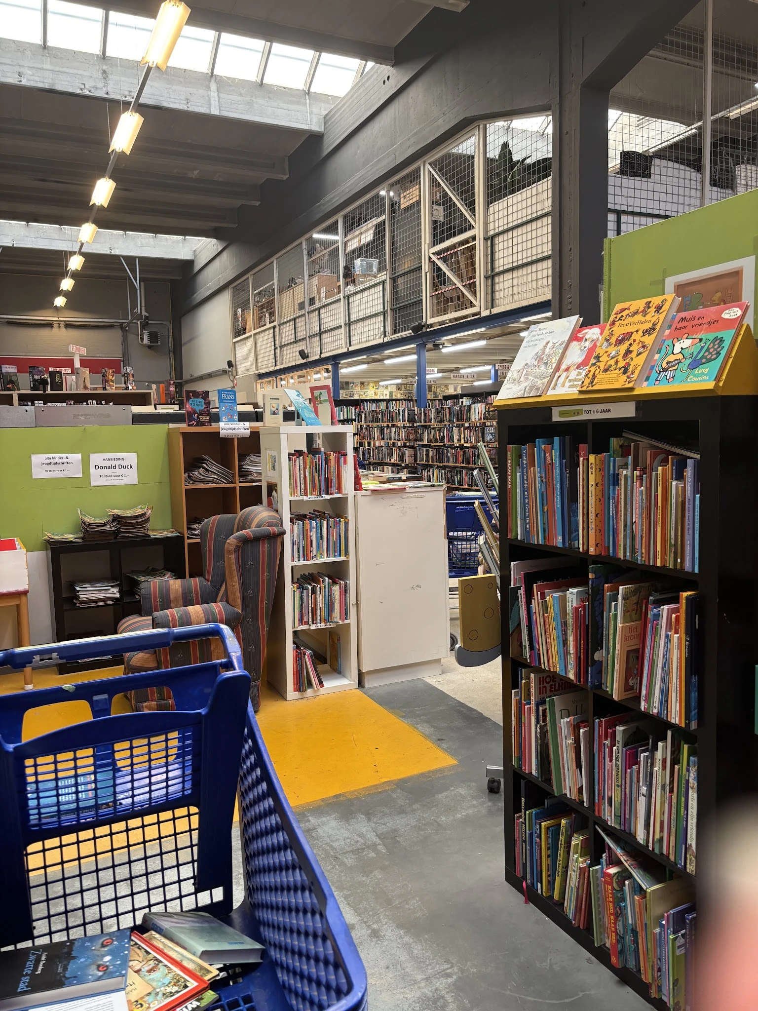 Winkelvloer met boekenrekken, blauwe winkelmandje en geel platform in kringloopcentrum