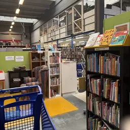 Winkelvloer met boekenrekken, blauwe winkelmandje en geel platform in kringloopcentrum