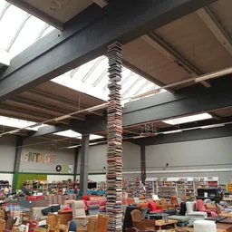 Interieur van kringloopwinkel met hoge plafonds, stalen constructie en een opvallende boekentoren in het midden, omgeven door